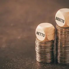 Dwie wieże monet, jedna z kostką "NETTO", druga z "BRUTTO". Różnica między nimi to nasza średnia krajowa netto.