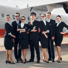 Grupa pilotów i stewardess w eleganckich mundurkach pozuje przed samolotem.