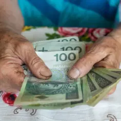Dłonie starszej osoby liczą banknoty 100 zł. Może to być pomocne przy analizie 14 emerytura tabela.