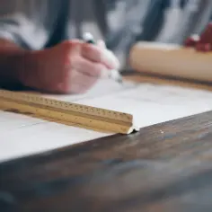 Architekt rysuje plany, zastanawiając się, ile zarabia architekt. Na stole leży linijka i zwój papieru.