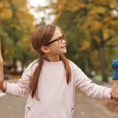 Dziewczynka w okularach trzyma za ręce dwoje dorosłych, tworząc obraz szczęśliwego związku partnerskiego.