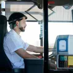 Mężczyzna za kierownicą autobusu, zastanawia się ile zarabia kierowca autobusu. Widoczny biletomat i siedzenie kierowcy.
