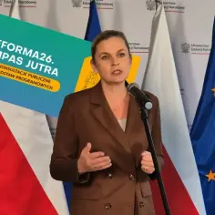 Minister edukacji przemawia na tle flag Polski i UE. Obok niej plansza "Reforma26. Kompas Jutra".