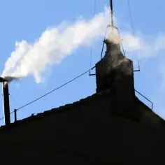Biały dym unosi się z komina na tle błękitnego nieba.