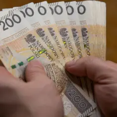 Dłonie trzymają plik banknotów 200 zł. Czy to już więcej niż najniższa krajowa netto?