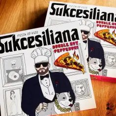 Dwie pizzy kizo "Sukcesiliana" z podwójnym pepperoni, ozdobione wizerunkiem kucharza z psem i płonącym kawałkiem pizzy.