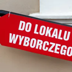 Czerwona strzałka z białym napisem "DO LOKALU WYBORCZEGO". Wskazuje drogę do miejsca, gdzie można oddać głos, przypominając o tym, ile trwa kadencja wójta.
