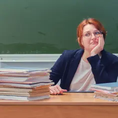 Nauczycielka zamyślona nad stertą prac, zastanawia się, ile zarabia nauczyciel.