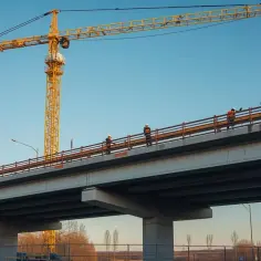 Budowa drogi z dźwigiem w tle. Pracownicy na moście, marzą o stawce godzinowej netto 2026.