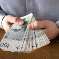 Dłonie trzymające stos banknotów 100 zł. Może to symbolizować zarobki z najlepiej płatnych zawodów.