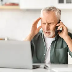 Zmartwiony mężczyzna rozmawia przez telefon, trzymając się za głowę. Czyżby czekał na pomoc od siły wyższej?