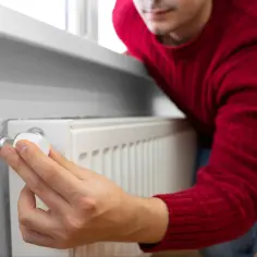 Mężczyzna reguluje termostat grzejnika, oszczędzając energię. Czy w 2026 roku będzie dostępny bon energetyczny?