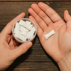 Dłonie trzymające pojemnik z białymi woreczkami nikotynowymi i jeden woreczek na dłoni. Czy snusy są legalne w Polsce?