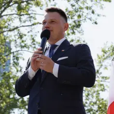 Sławomir Mentzen przemawia na tle drzew i nowoczesnego budynku, mówiąc o swoim majątku.