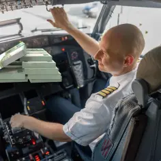 Pilot w kokpicie z plikami banknotów euro. Czy to odzwierciedla, ile zarabia pilot samolotu?