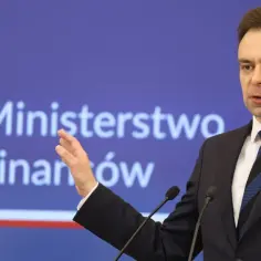 Minister finansów przemawia na tle logo Ministerstwa Finansów.