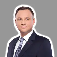 Prezydent Andrzej Duda w garniturze, z biało-czerwoną flagą na klapie. Jego uśmiech sugeruje, że właśnie podjął ważną decyzję, być może dotyczącą ułaskawienia prezydenta Nawrockiego.