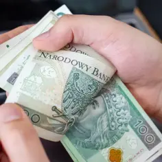 Dłonie trzymają plik banknotów 100 zł. Może to być zapłata za usługi, np. opłata reprograficzna.