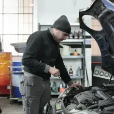 Mechanik w czapce z daszkiem sprawdza silnik. Zastanawiasz się, ile zarabia mechanik?