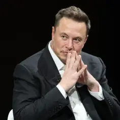 Elon Musk, uważany za najbogatszego człowieka na świecie, w garniturze, z dłońmi złożonymi przed twarzą.