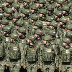 Żołnierze w rosyjskich mundurach, z flagami na hełmach, stoją w zwartym szyku. Ich twarze wyrażają powagę, być może myśląc o stratach Rosjan.
