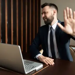 Mężczyzna w garniturze wykonuje gest "stop" przed laptopem, jakby protestował przeciwko pracy. To jego forma strajku włoskiego.
