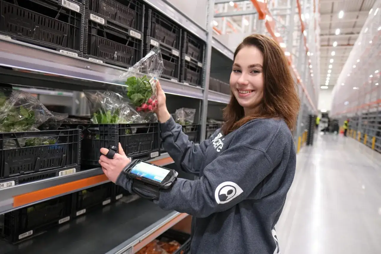 Uśmiechnięta pracownica kompletuje zamówienie w magazynie. To praca w Holandii, gdzie nowoczesne technologie ułatwiają codzienne zadania.