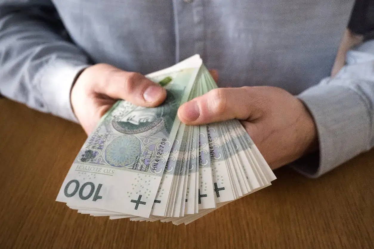 Dłonie trzymające stos banknotów 100 zł. Może to symbolizować zarobki z najlepiej płatnych zawodów.