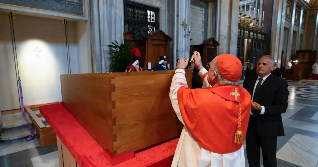 Kardynał w stroju liturgicznym błogosławi trumnę podczas uroczystości pogrzebowych. Papież Franciszek jest obecny.