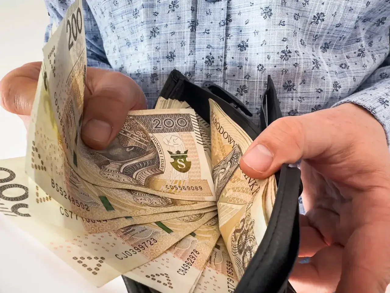 Ręce trzymają portfel z banknotami 200 zł. To nagroda jubileuszowa za 40 lat pracy w budżetówce.
